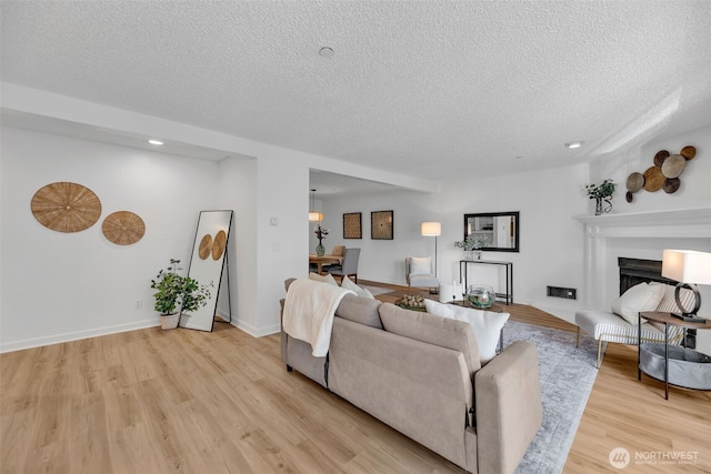 living area with light wood-style flooring, baseboards, and a textured ceiling