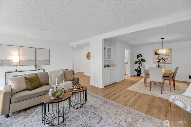 living room featuring light wood-style flooring, baseboards, and a textured ceiling