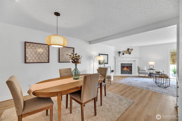 dining room featuring light wood-style flooring, a fireplace with flush hearth, baseboards, and a textured ceiling