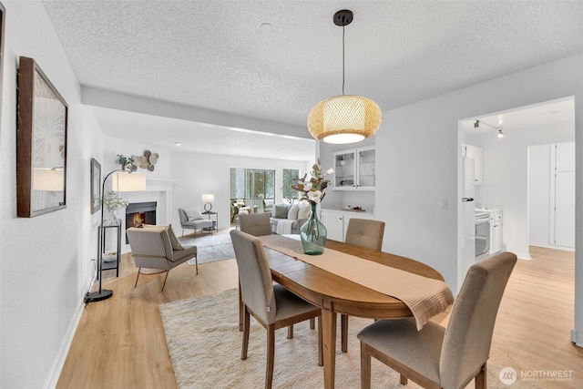 dining area with light wood-style flooring, a warm lit fireplace, and a textured ceiling