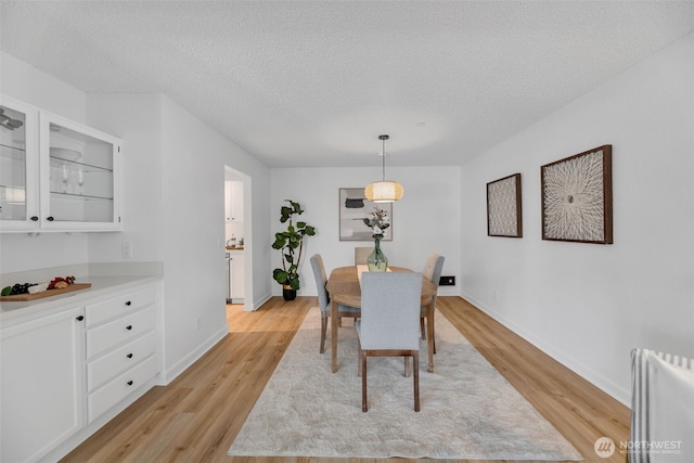 dining space with light wood-style flooring, a textured ceiling, and baseboards