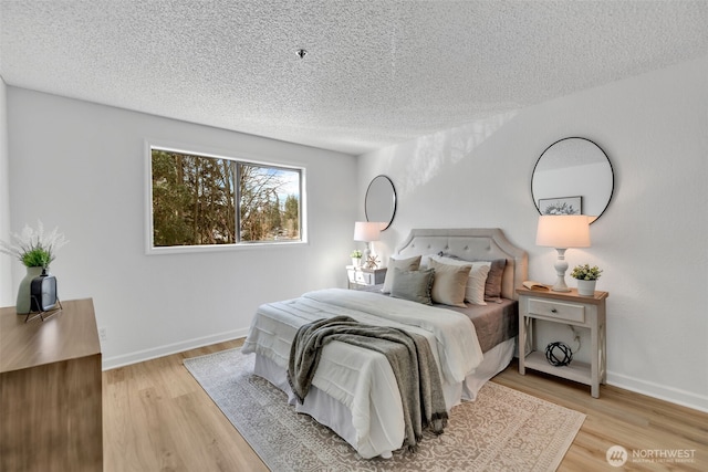 bedroom featuring baseboards, light wood-type flooring, and a textured ceiling