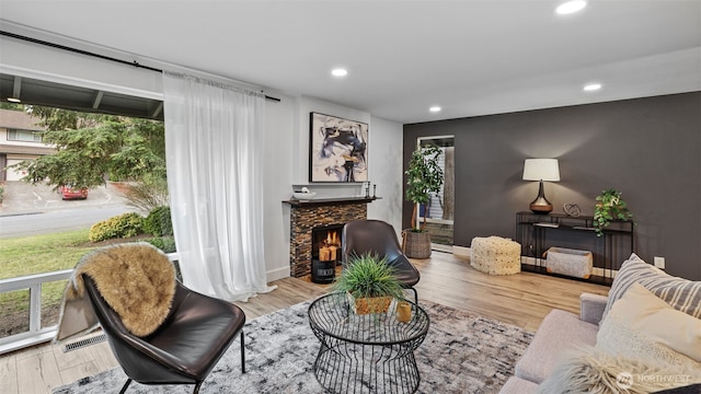 living room featuring a stone fireplace, wood finished floors, and a healthy amount of sunlight