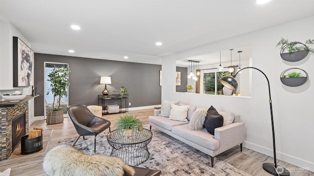 living room with recessed lighting, a warm lit fireplace, light wood-type flooring, and baseboards