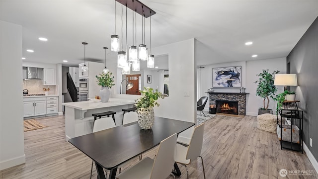 dining area with light wood-type flooring, recessed lighting, a fireplace, baseboards, and stairs