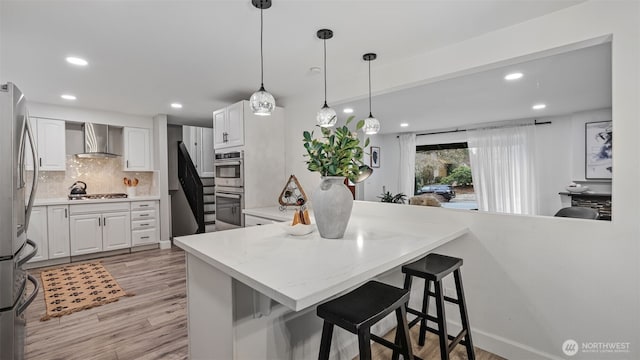 kitchen with a breakfast bar, stainless steel appliances, decorative backsplash, white cabinets, and wall chimney range hood