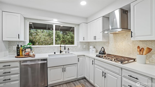 kitchen with light countertops, stainless steel appliances, white cabinetry, wall chimney exhaust hood, and a sink