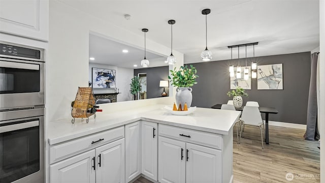 kitchen with double oven, light countertops, a peninsula, light wood-style floors, and white cabinetry