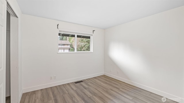 unfurnished room with wood finished floors, visible vents, and baseboards