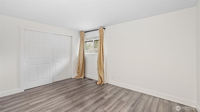 unfurnished bedroom featuring light wood finished floors, baseboards, and a closet