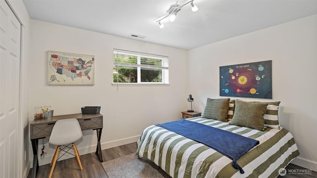 bedroom featuring visible vents, baseboards, wood finished floors, and rail lighting