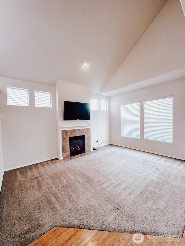 unfurnished living room with baseboards, high vaulted ceiling, carpet flooring, and a tiled fireplace