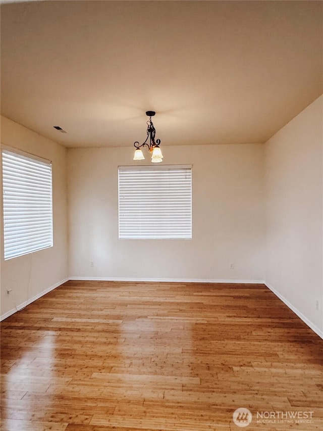 unfurnished room featuring an inviting chandelier, wood finished floors, and baseboards