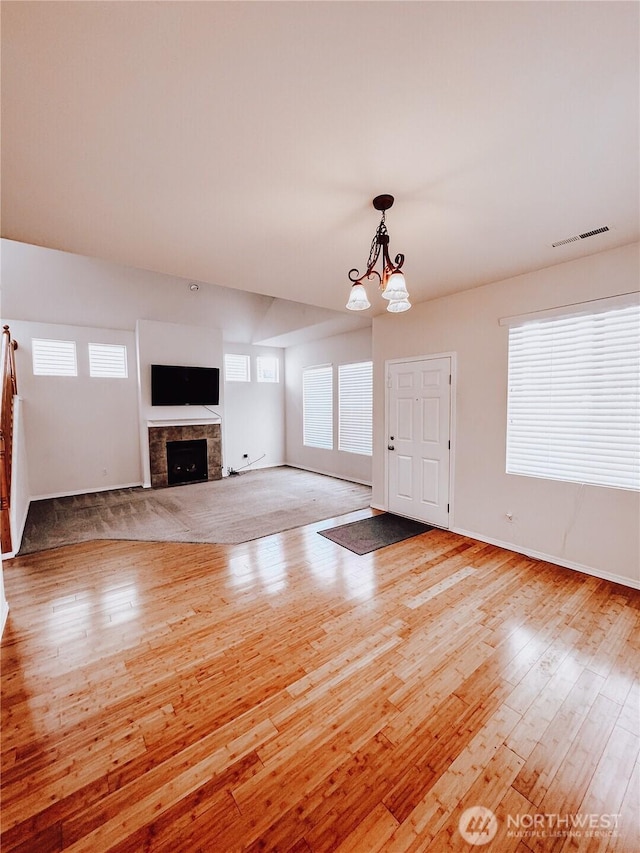 unfurnished living room featuring light wood-type flooring, visible vents, a chandelier, and a fireplace