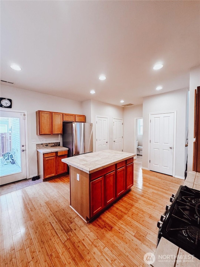 kitchen with light wood-type flooring, visible vents, tile counters, and freestanding refrigerator