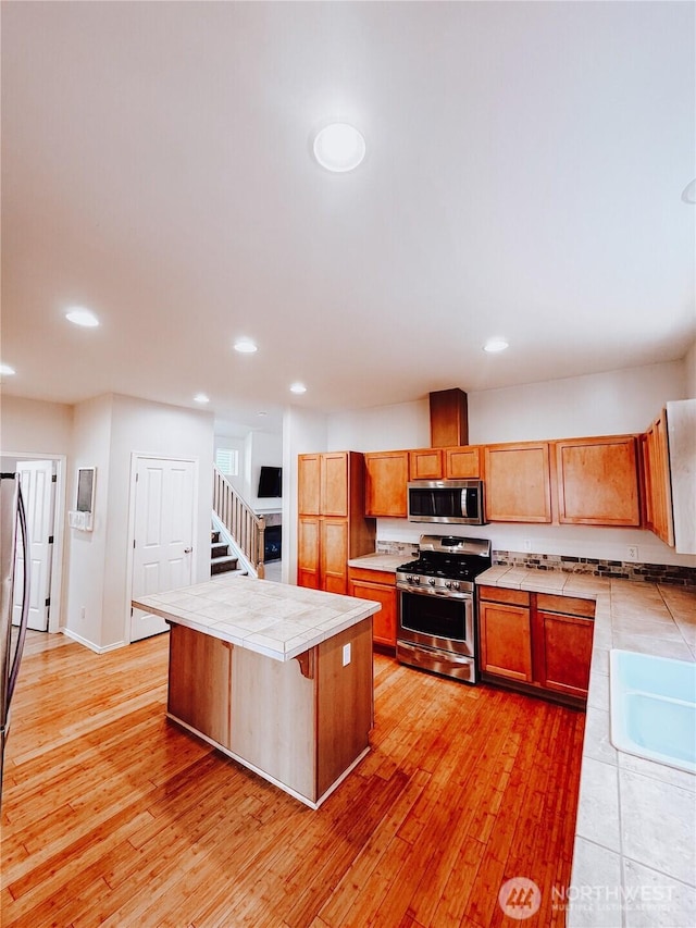 kitchen with a sink, stainless steel appliances, light wood-type flooring, and tile counters