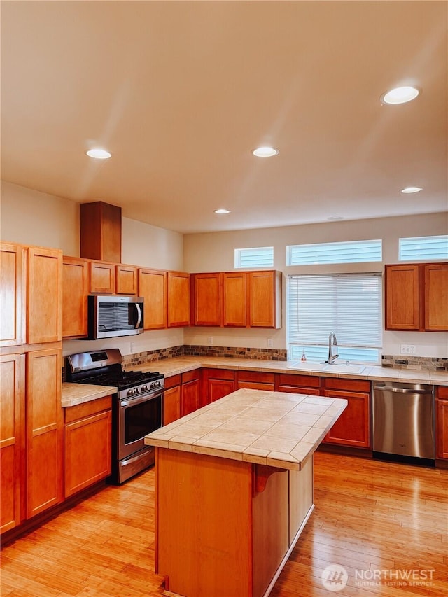 kitchen with a center island, tile counters, light wood-type flooring, appliances with stainless steel finishes, and a sink