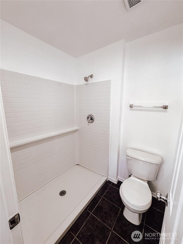 bathroom featuring tile patterned flooring, toilet, visible vents, and tiled shower