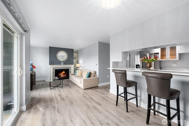 living area with baseboards, light wood finished floors, and a lit fireplace