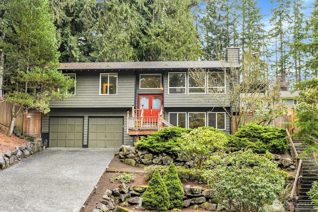 split foyer home featuring aphalt driveway, an attached garage, a chimney, and fence