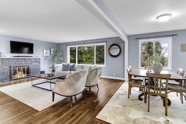 living room with a stone fireplace, wood finished floors, baseboards, and a wealth of natural light