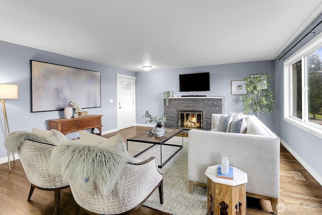 living room featuring a glass covered fireplace, wood finished floors, and baseboards