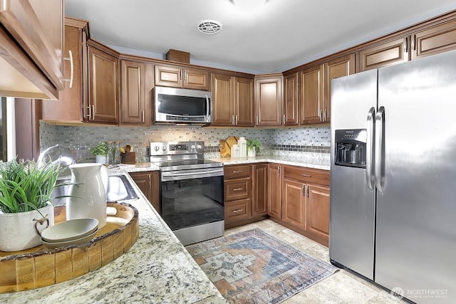 kitchen featuring light stone counters, visible vents, brown cabinets, appliances with stainless steel finishes, and tasteful backsplash