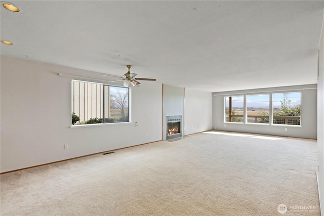 unfurnished living room with visible vents, a fireplace with flush hearth, ceiling fan, and carpet flooring