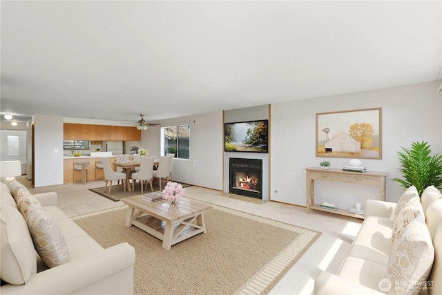 living room featuring light carpet, a ceiling fan, and a fireplace with flush hearth