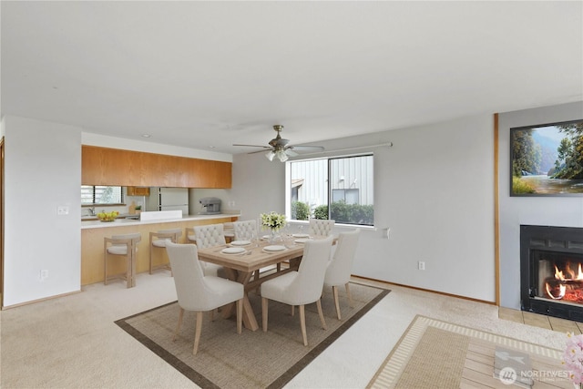 dining area with a wealth of natural light, light colored carpet, baseboards, and a lit fireplace