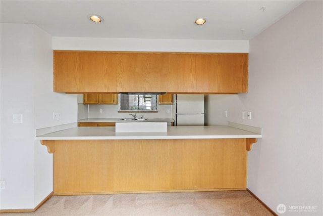 kitchen featuring light countertops, recessed lighting, a peninsula, freestanding refrigerator, and a sink