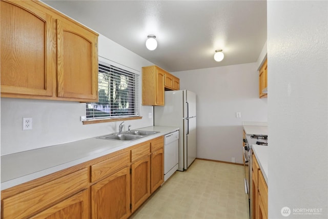 kitchen featuring baseboards, light floors, light countertops, white appliances, and a sink