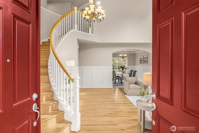 foyer with light wood-type flooring, stairway, arched walkways, wainscoting, and a chandelier