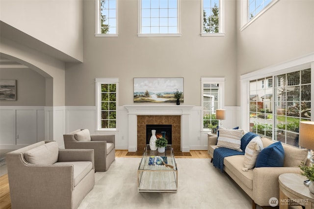 living area with light wood-type flooring, arched walkways, wainscoting, and a tile fireplace