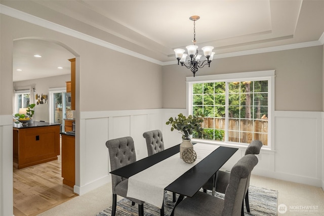 dining area with arched walkways, a chandelier, wainscoting, and a tray ceiling