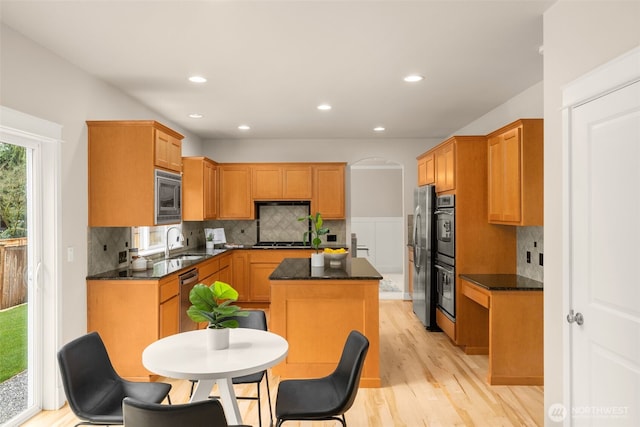 kitchen featuring backsplash, a kitchen island, light wood-style flooring, stainless steel appliances, and a sink