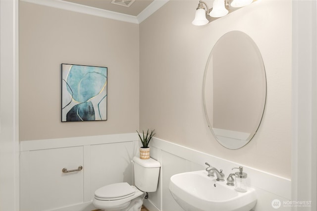 half bath featuring a sink, visible vents, toilet, and crown molding