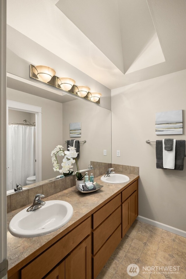 full bathroom featuring double vanity, toilet, baseboards, and a sink