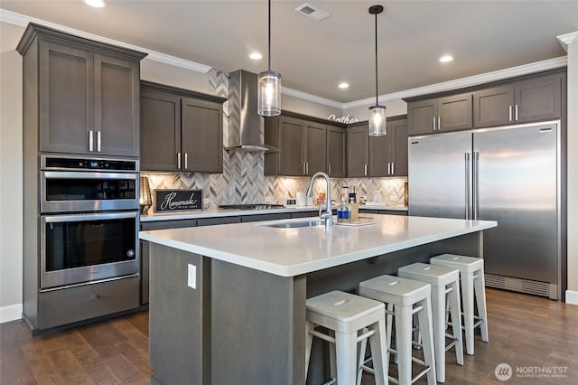 kitchen with visible vents, crown molding, wall chimney range hood, stainless steel appliances, and a sink