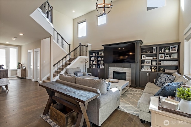 living room with stairs, a stone fireplace, recessed lighting, a high ceiling, and dark wood-style floors