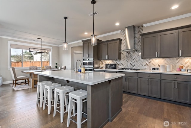 kitchen featuring visible vents, ornamental molding, stainless steel appliances, light countertops, and wall chimney range hood