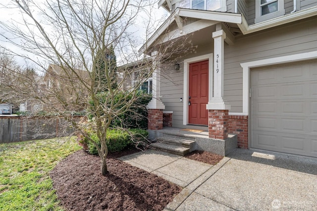 doorway to property featuring fence, brick siding, and a garage