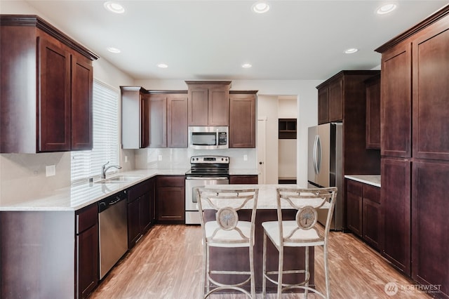 kitchen featuring a sink, a kitchen breakfast bar, appliances with stainless steel finishes, and light wood finished floors