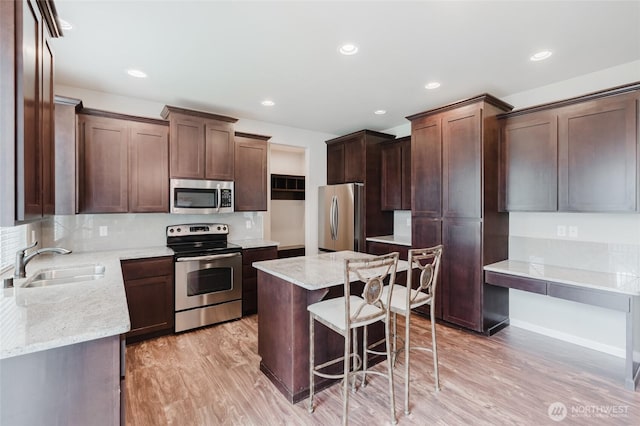 kitchen featuring a kitchen island, a kitchen bar, light wood-style floors, stainless steel appliances, and a sink