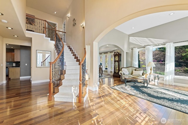 foyer featuring stairway, wood finished floors, arched walkways, and baseboards