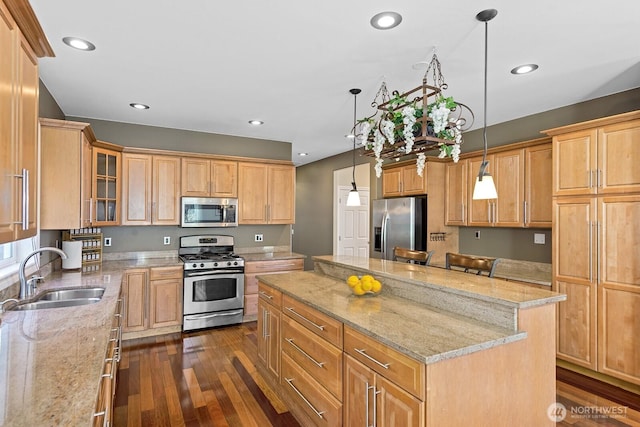 kitchen with light stone counters, dark wood-style floors, a sink, appliances with stainless steel finishes, and a center island