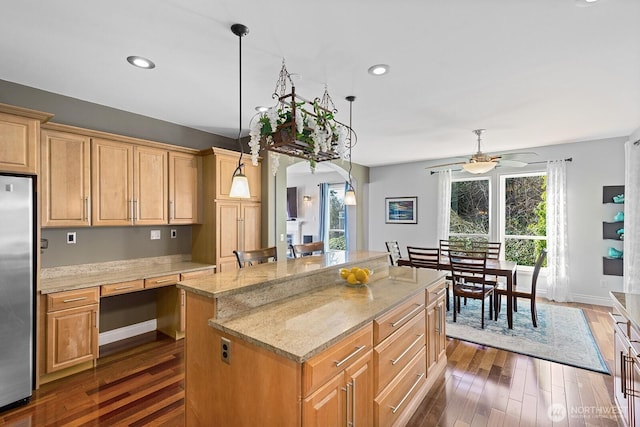 kitchen with light stone counters, a ceiling fan, dark wood finished floors, stainless steel refrigerator, and a center island