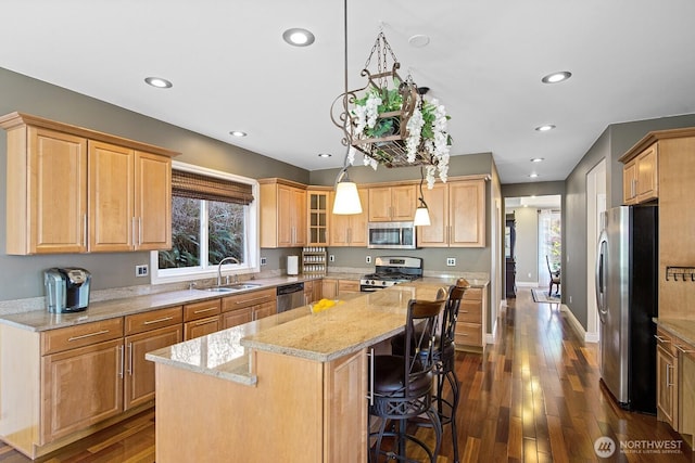 kitchen featuring a sink, a kitchen island, light stone counters, appliances with stainless steel finishes, and dark wood-style flooring