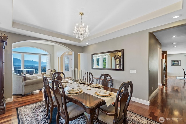 dining space with a chandelier, a raised ceiling, baseboards, and hardwood / wood-style floors