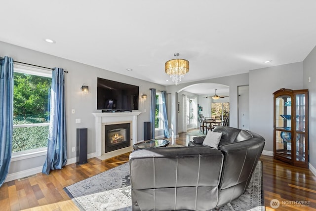 living area with arched walkways, plenty of natural light, wood finished floors, and a tiled fireplace